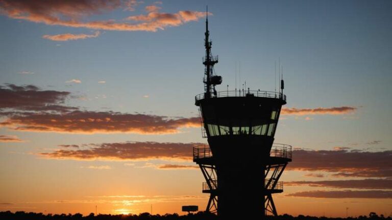 Silhouette of an Australian air traffic control tower at sunset with radar antennas against a clear sky